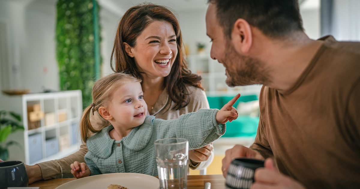 Fröhliche Familie mit kleinem Kind sitzt gemeinsam am Frühstückstisch und lacht – entspannte Morgenstimmung im modernen Zuhause.