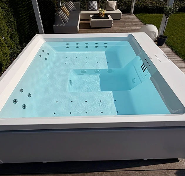Nahaufnahme der Innenwanne eines klaren, türkisfarbenen Whirlpools bei Tageslicht. Die Wanne zeigt zahlreiche Massagedüsen und das Filtersystem, platziert auf einem Holzdeck.